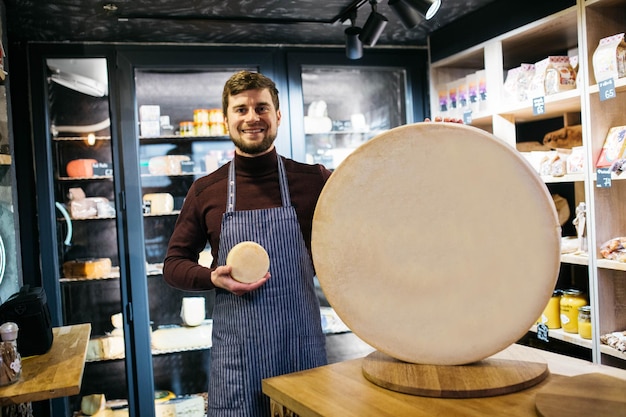 Queijo de mesa de madeira na fábrica de queijo O homem fica à esquerda do queijo Um homem segura um pedaço nas mãos