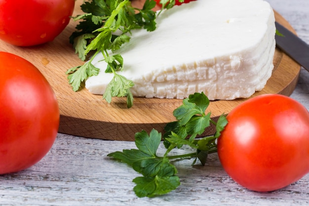 Queijo de salmoura branco, faca, salsa, tomate em um fundo de tábuas de madeira