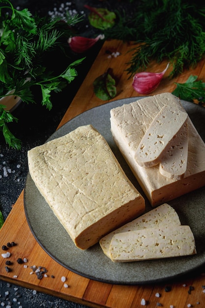 Queijo de soja tofu fatiado em uma tábua de corte com especiarias e legumes de manjericão