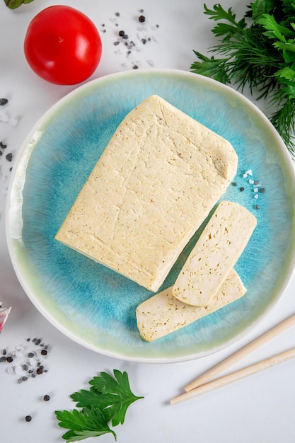 Queijo de soja tofu fatiado em uma tábua de corte com especiarias e legumes de manjericão