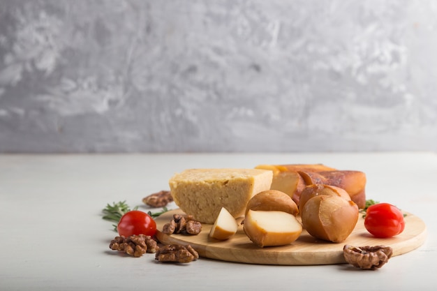 Queijo defumado e vários tipos de queijo na placa de madeira, sobre um fundo cinza e branco