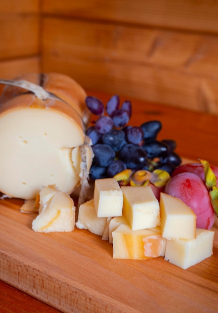 Queijo defumado grego tradicional Metsovone em uma placa de madeira com uvas e caquis na Grécia