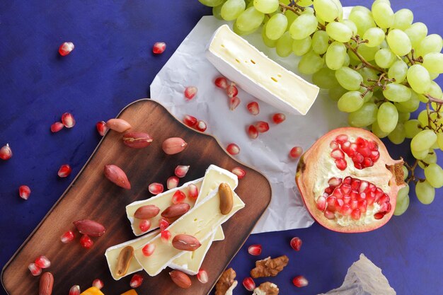 Queijo delicioso em tábua de madeira e papel pergaminho fecha Camembert com sementes de romã, uvas verdes e nozes sobre fundo azul