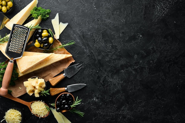 Queijo duro com azeitonas e faca de queijo em fundo de pedra preta Parmesão Vista superior Espaço livre para o seu texto