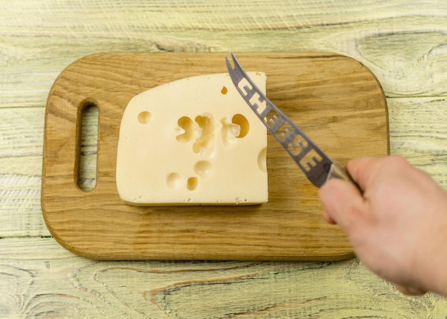 Queijo e mão com uma faca para cortar queijo