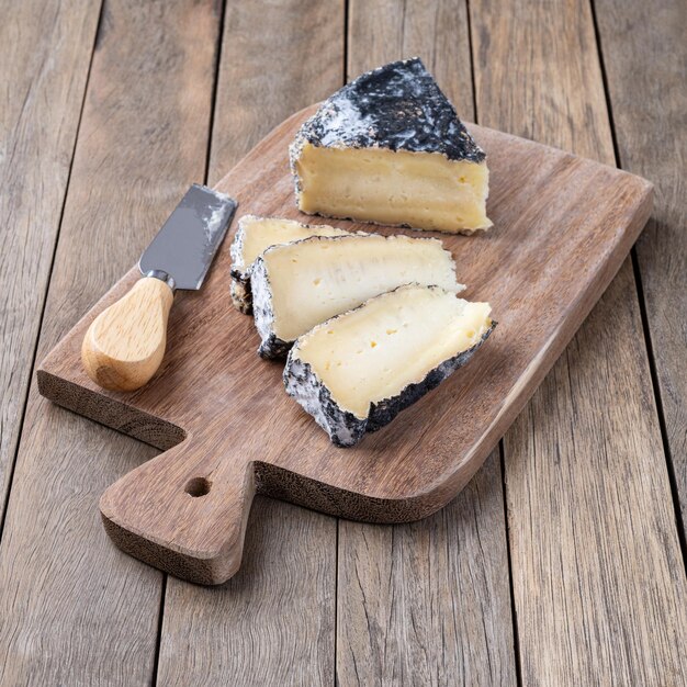 Foto queijo envelhecido a carvão com fatias sobre mesa de madeira