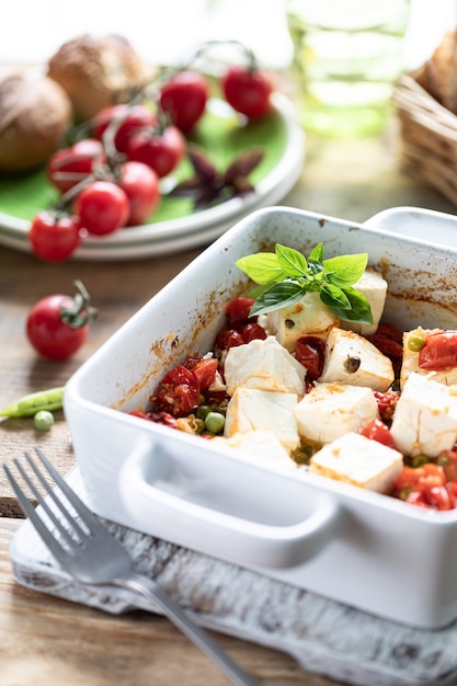 Queijo feta assado com tomate cereja com manjericão e azeite. Cozinha nacional grega.
