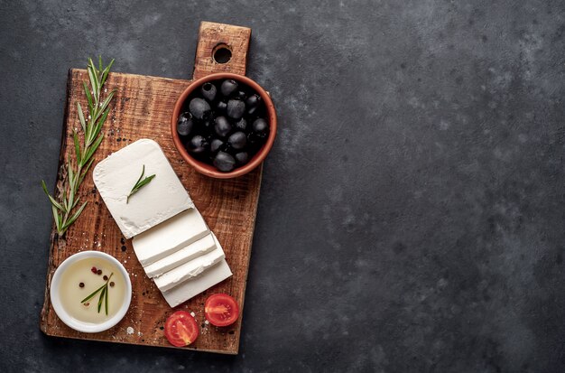 queijo feta, com alecrim, tomate, azeitonas em um fundo de pedra. vista superior com espaço de cópia para o seu texto