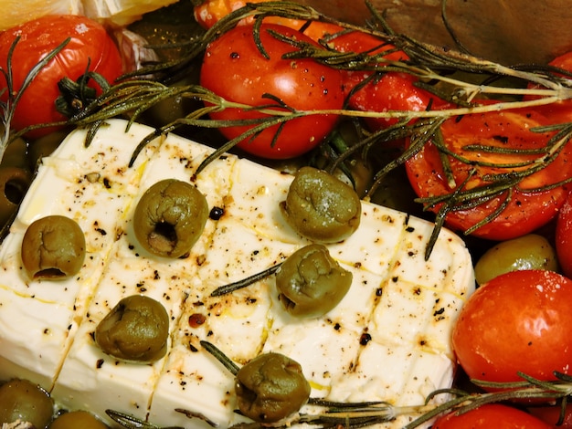 Queijo feta com azeitonas, alecrim e tomate cereja em papel vegetal.