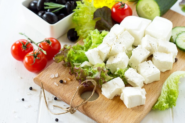 Foto queijo feta e azeitonas pretas cozinhando salada qreek com legumes frescos em uma mesa de madeira branca