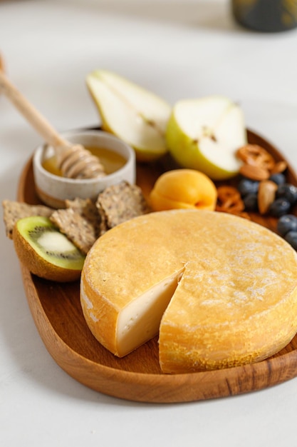 Queijo francês Reblochon na placa de madeira com frutas e mel Prato de queijo Queijo de corte