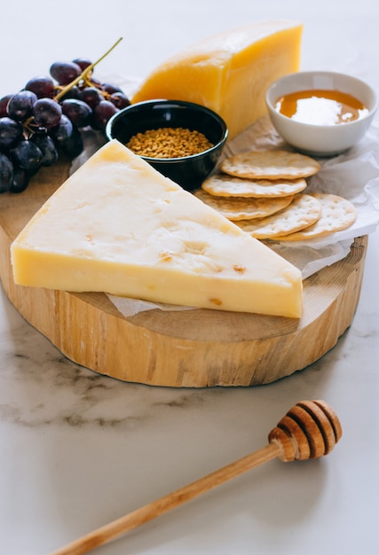 Queijo gruyere, uvas, nozes, mel e bolacha na placa de madeira em mármore