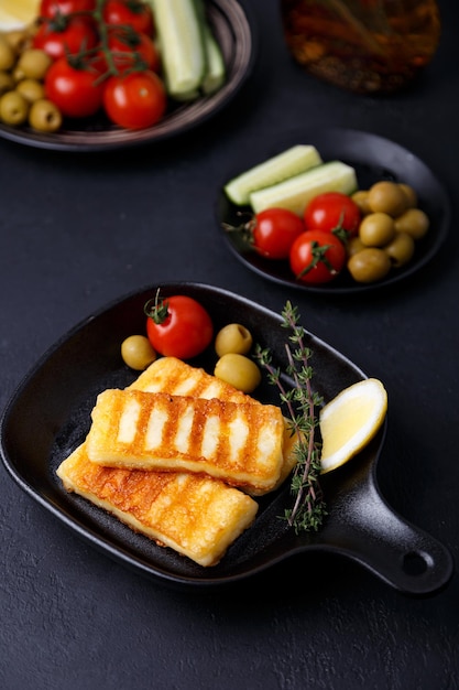 Queijo halloumi grelhado em uma panela preta com azeitonas tomates pepinos tomilho e limão queijo tradicional do mediterrâneo oriental closeup de foco seletivo de fundo preto