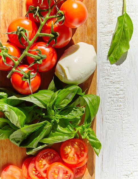 Queijo mussarela de búfala com tomate cereja, folhas de manjericão verde, sobre fundo de textura rústica