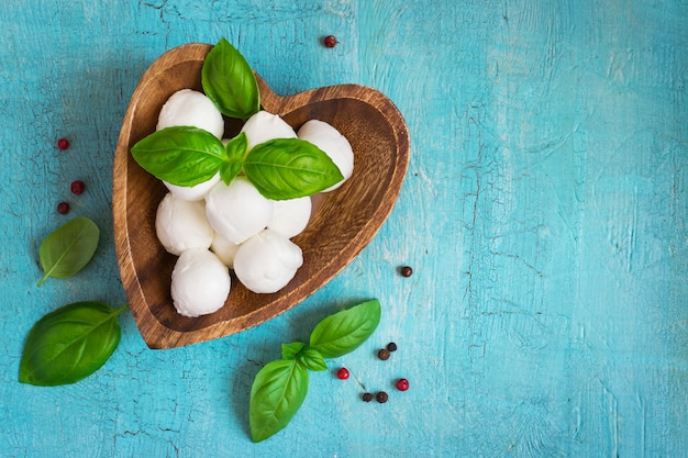 Queijo mussarela e manjericão em uma tigela de madeira sobre uma mesa turquesa. Conceito de cozinha italiana. Vista superior com espaço de cópia