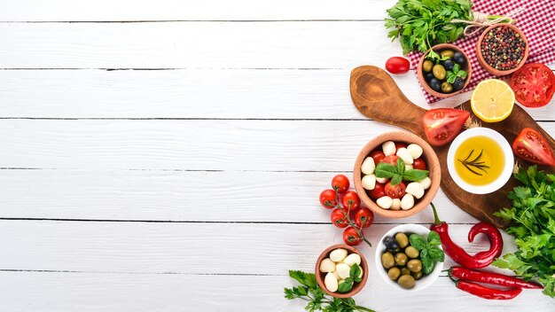 Queijo mussarela tomate cereja manjericão folhas óleo azeitonas pimenta Salada caprese Em uma mesa de madeira branca Espaço livre para texto