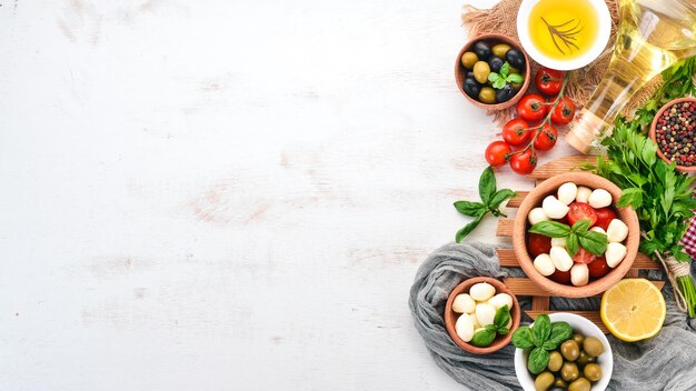 Queijo mussarela tomate cereja manjericão folhas óleo azeitonas pimenta Salada caprese Em uma mesa de madeira branca Espaço livre para texto