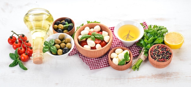 Queijo mussarela tomate cereja manjericão folhas óleo azeitonas pimenta salada caprese em uma mesa de madeira branca espaço livre para texto