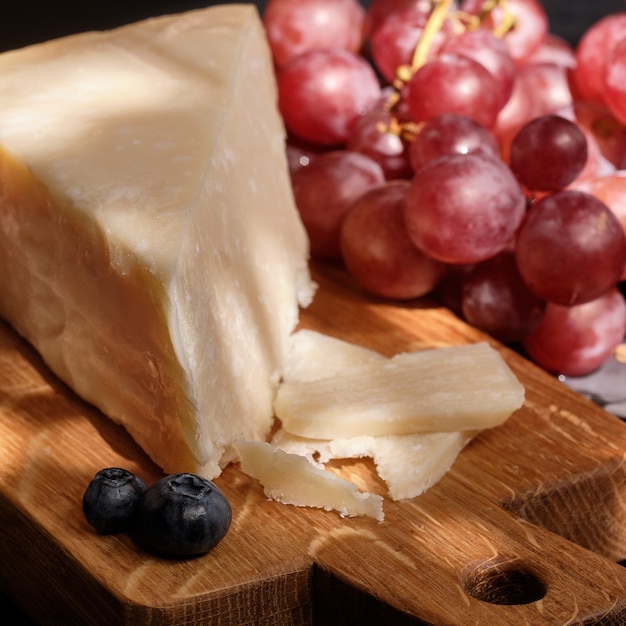 Foto queijo parmigiano na tábua de madeira com bagas de uva