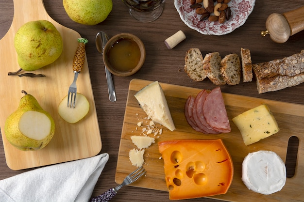 Queijo, presunto, peras e pão sobre fundo de madeira