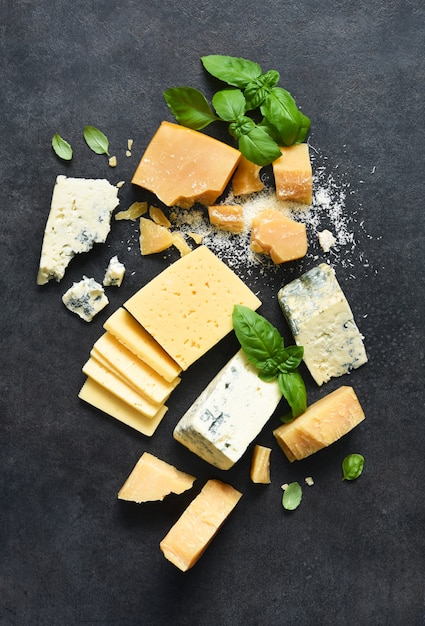 Queijo, queijo azul, parmesão e manjericão em uma mesa de concreto preta.