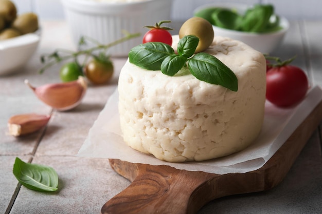 Queijo ricota Queijo ricota caseiro com tomates de manjericão alho e azeitonas verdes em brochura de pergaminho e suporte sobre fundo de azulejos bege velhos Comida italiana Foco seletivo