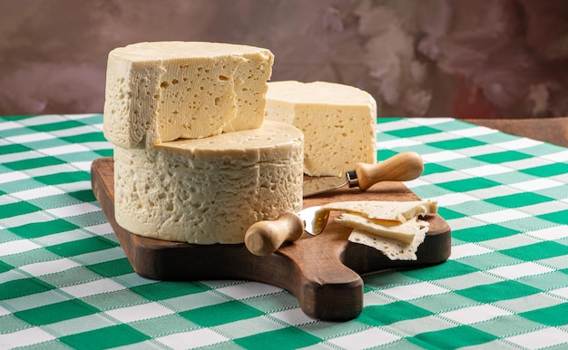 Queijo semi-curado do Brasil disposto em uma tábua rústica sobre uma toalha de mesa quadriculada verde e branca, foco seletivo.