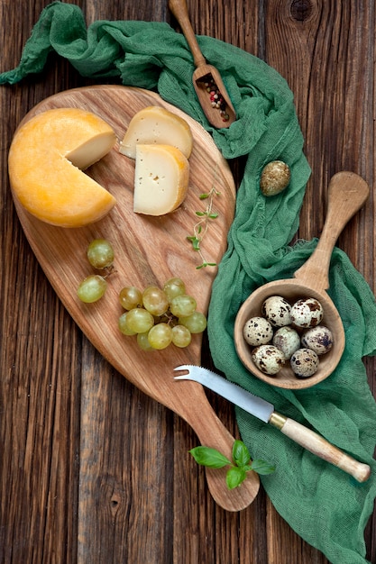 Queijo, uvas e ovos de codorna em fundo de madeira rústico.