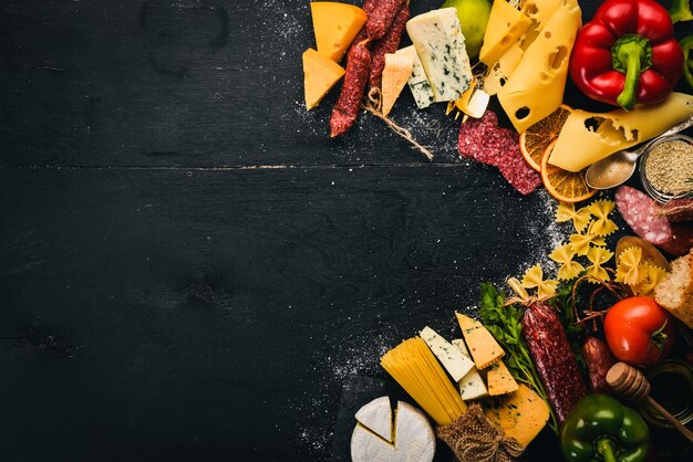 Queijos variados enchidos vinhos especiarias tradicionais e legumes frescos em um fundo de madeira queijo brie queijo azul gorgonzola fuete salame cozinha italiana e espanhola espaço livre