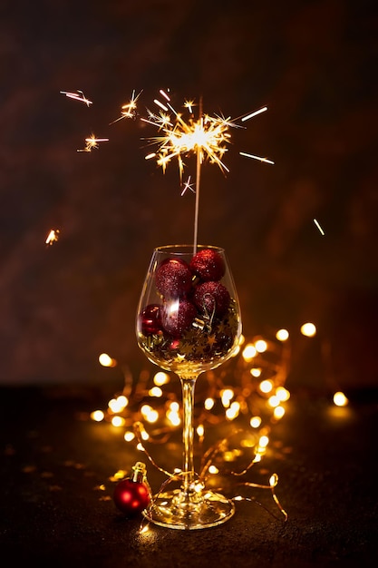 Queima de fogos de artifício de bengala em uma taça de vinho com bolas vermelhas de Natal