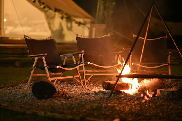 Queima de fogueira e cadeiras dobráveis perto da barraca de acampamento à noite