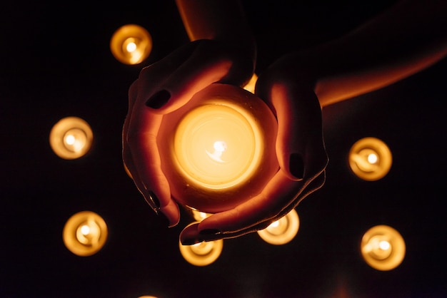 Queima de velas. Vela em mãos femininas. Muitas velas acesas à noite. Muitas chamas de velas brilhando.