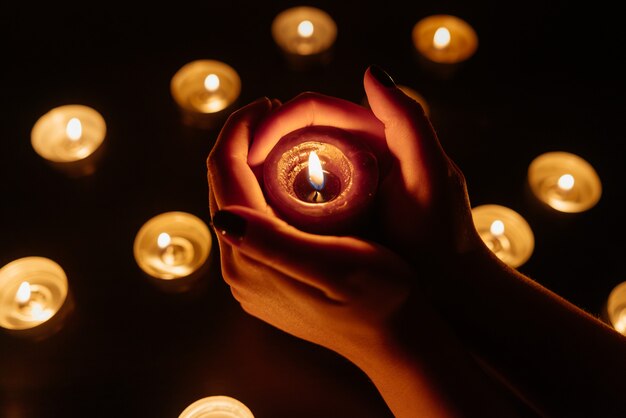 Queima de velas. Vela em mãos femininas. Muitas velas acesas à noite. Muitas chamas de velas brilhando.