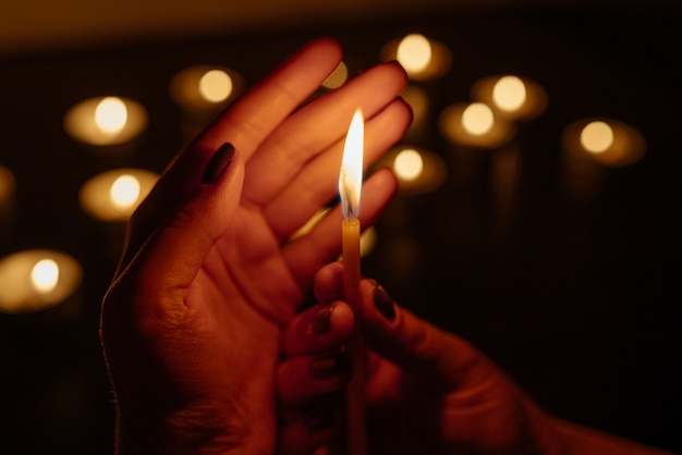 Queima de velas. Vela em mãos femininas. Muitas velas acesas à noite. Muitas chamas de velas brilhando.