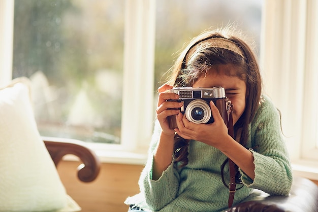 Quem sabe onde seu hobby pode levá-la Foto de uma garotinha tirando fotos com uma câmera vintage em casa