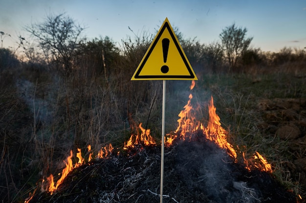 Quema de hierba seca y señal de advertencia con signo de exclamación advierte sobre peligroso en el campo con fuego Concepto de ecología y desastre natural