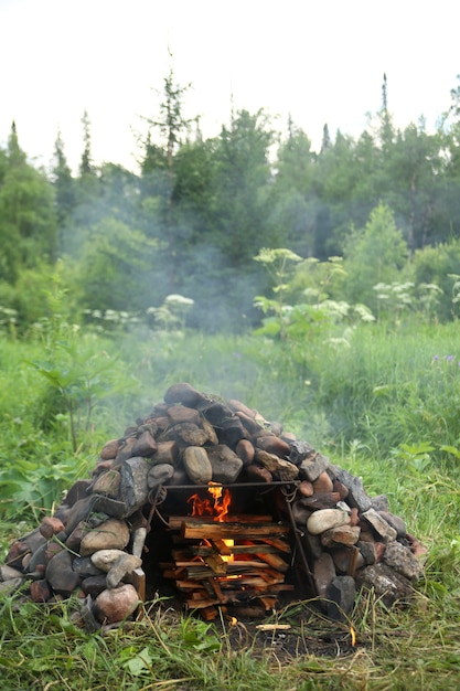 Foto quema de leña en una estufa construida con piedras grandes al aire libre en el bosque