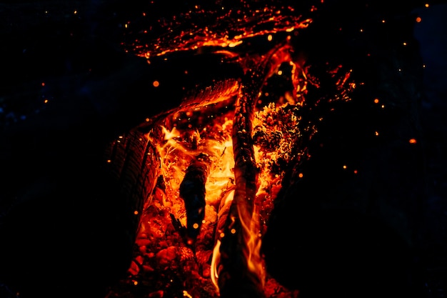 Quema de madera por la noche. Fogata en el campamento turístico en la naturaleza en las montañas. Llama y fuego chispas en noche oscura abstracta. Cocinar barbacoa al aire libre.