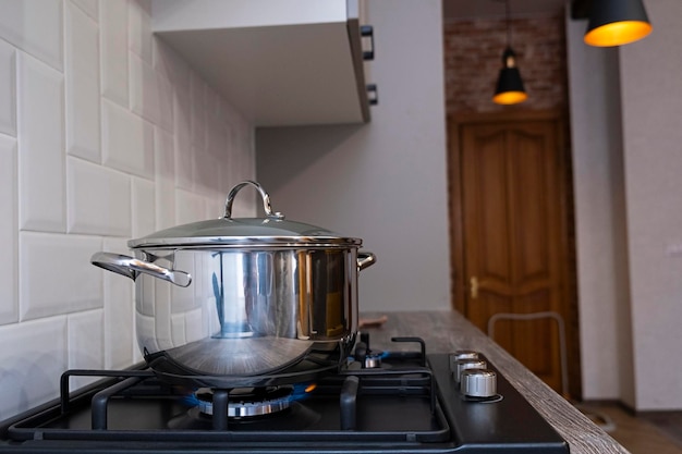 Quemador de gas ardiendo con llamas azules en la estufa de gas negro de la cocina con una olla de acero de gasolina con efecto bokeh