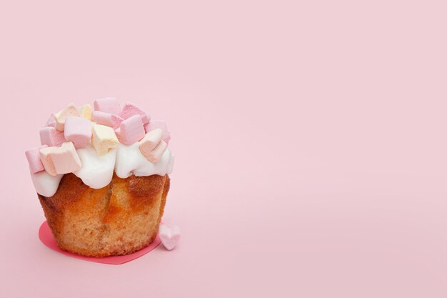 Foto queque com corações de marshmallow em um fundo rosa com um pequeno coração perto do muffin