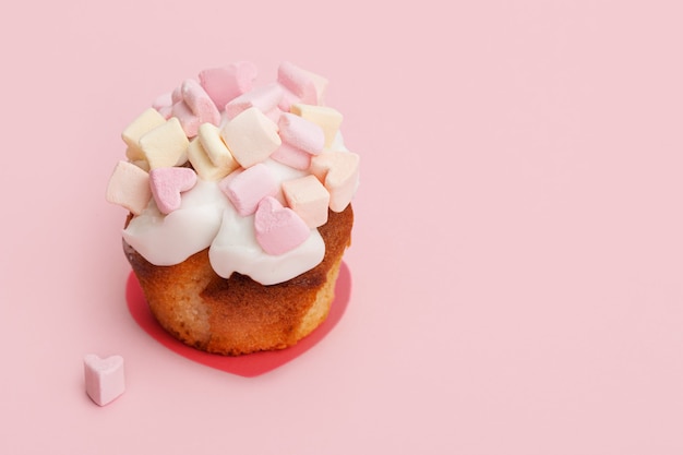 queque com corações de marshmallow em um fundo rosa com um pequeno coração perto do muffin