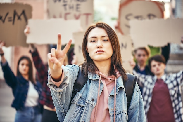 Queremos paz, la mujer joven está mostrando el signo de la pieza mientras está de pie frente a la hembra