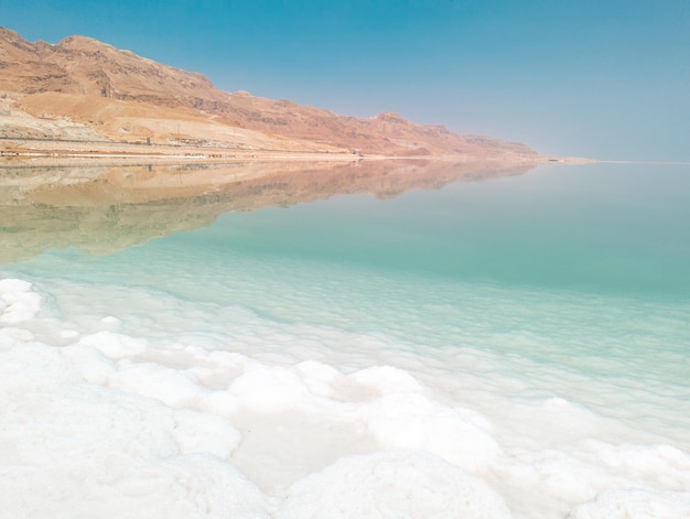 Querformat auf Salzkristallformationen aus dem Toten Meer klares cyan-grünes Wasser und Berge am Strand von Ein Bokek Israel
