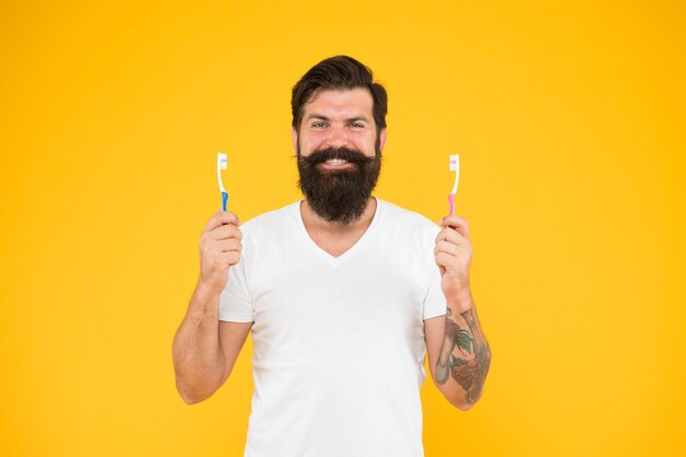 Queria dentes felizes Hipster feliz segura escovas fundo amarelo Homem barbudo feliz sorrindo com escovas de dentes Cuidados dentários Saúde e higiene dos dentes Rotina diária Os canais radiculares fazem dentes felizes