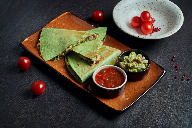 Quesadilla assado apetitoso com frango picado de queijo em tortilla verde em um prato de cerâmico em uma mesa preta. cozinha mexicana moderna.