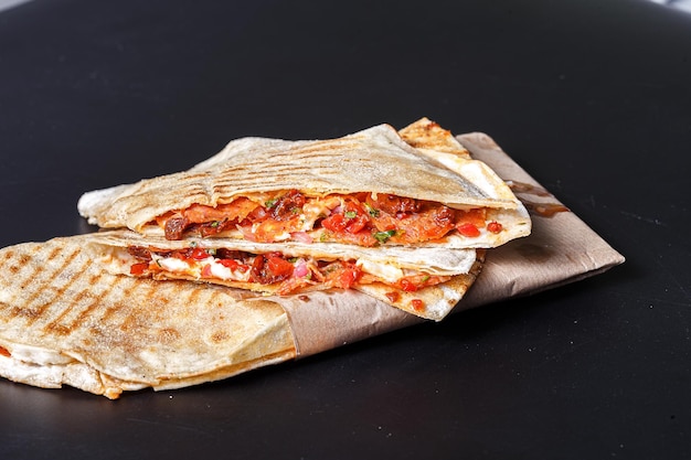 quesadilla mexicana, casera, en papel envolvente, sobre un fondo negro aislado