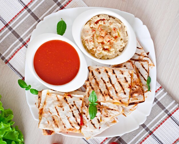 Quesadilla mexicana en rebanadas con verduras y salsas en la mesa