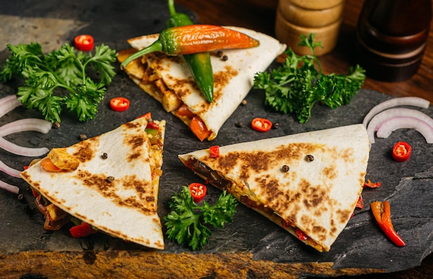 Quesadilla mit Hühnchen und Peperoni, geschweiften Petersilienblättern und zwei Flaschen scharfer Soße