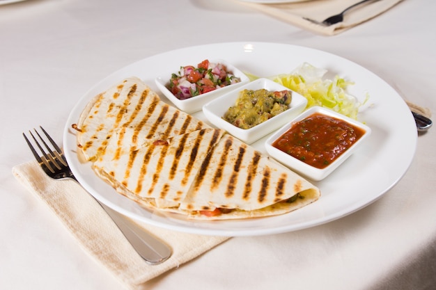 Quesadilla a la parrilla en un plato con variedad de salsas y aderezos en el lugar