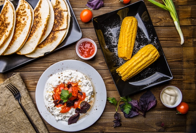 Quesadilla, Salat mit Hüttenkäse und Tomaten, Mais zwei auf hölzerner Tabelle.